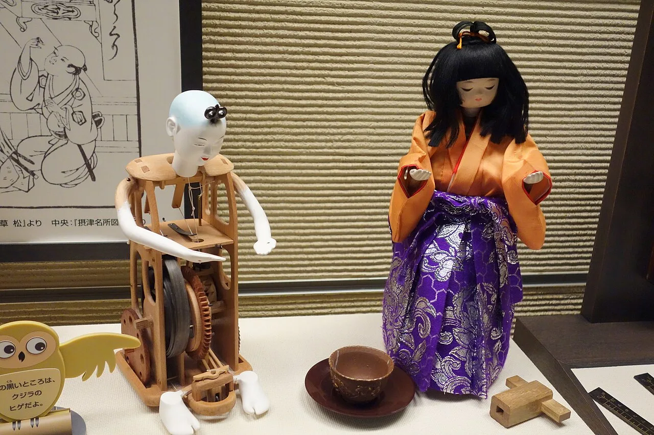 Two replica tea-serving dolls, one dressed and one with its wooden body opened to show the gears inside