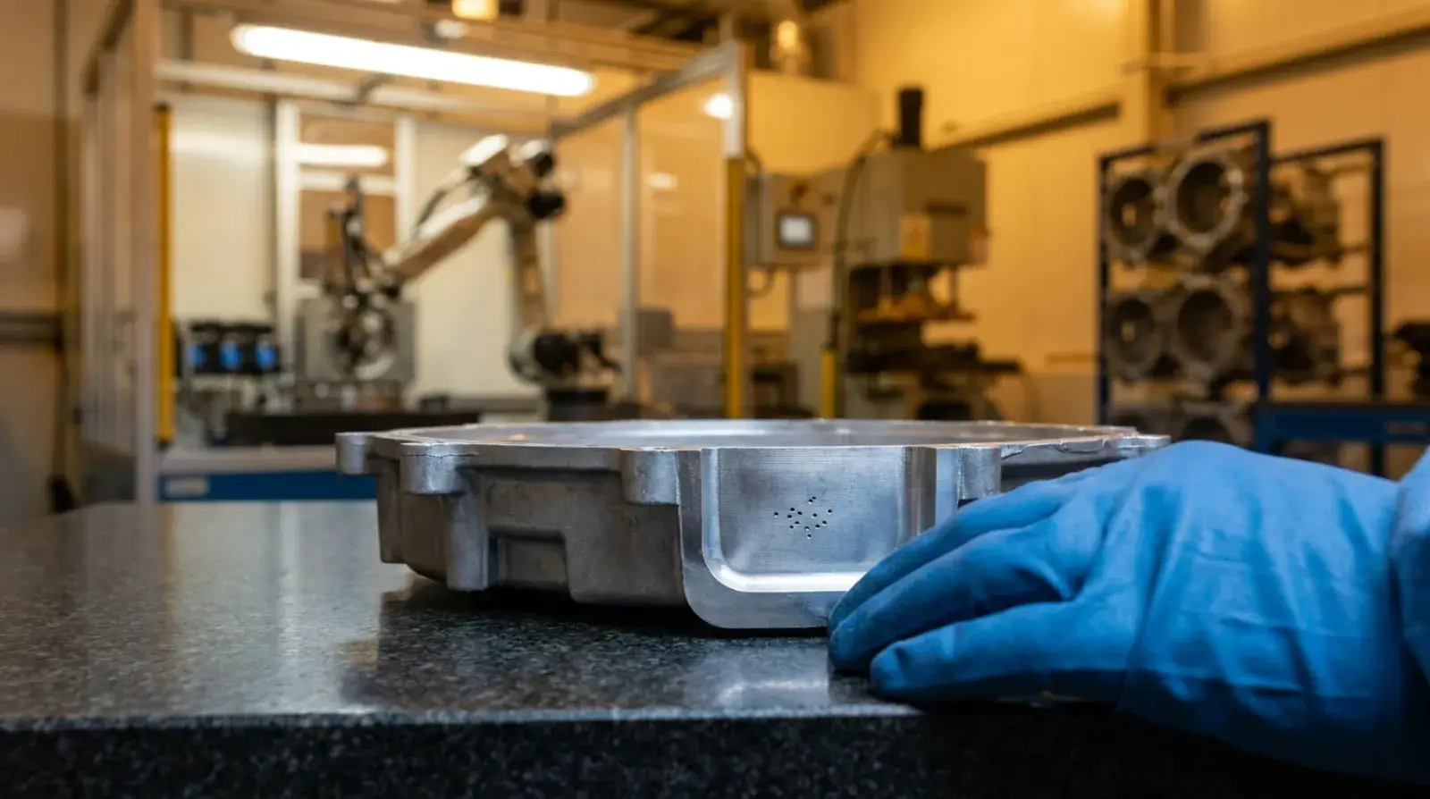 Gloved hand inspecting a freshly cast aluminum housing resting on a granite surface plate
