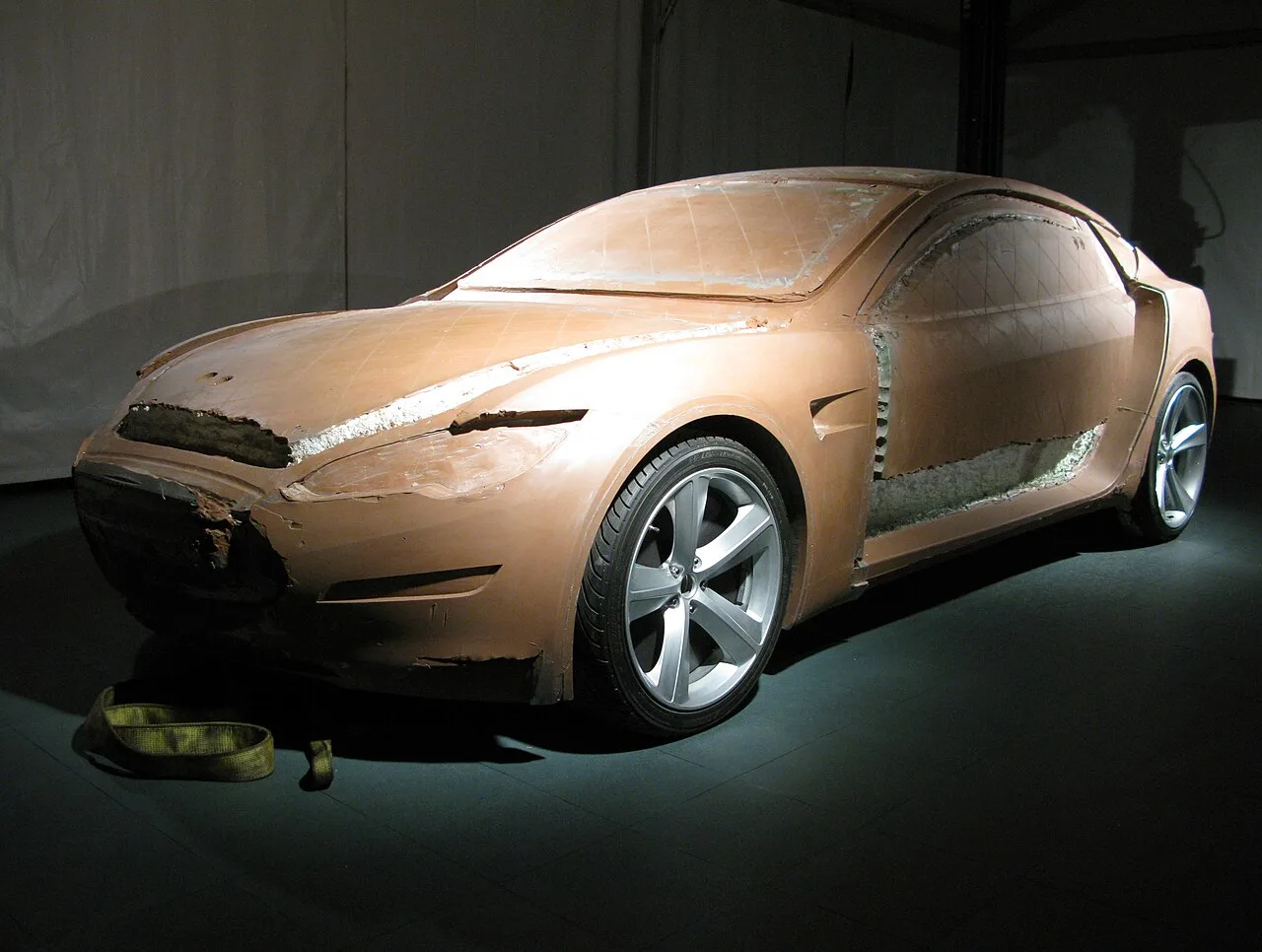 A full-size clay model of a sedan, partly finished, under studio lights