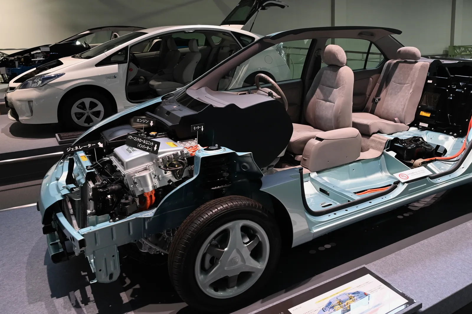 A cutaway of a first-generation Toyota Prius showing the engine bay and the battery behind the rear seat