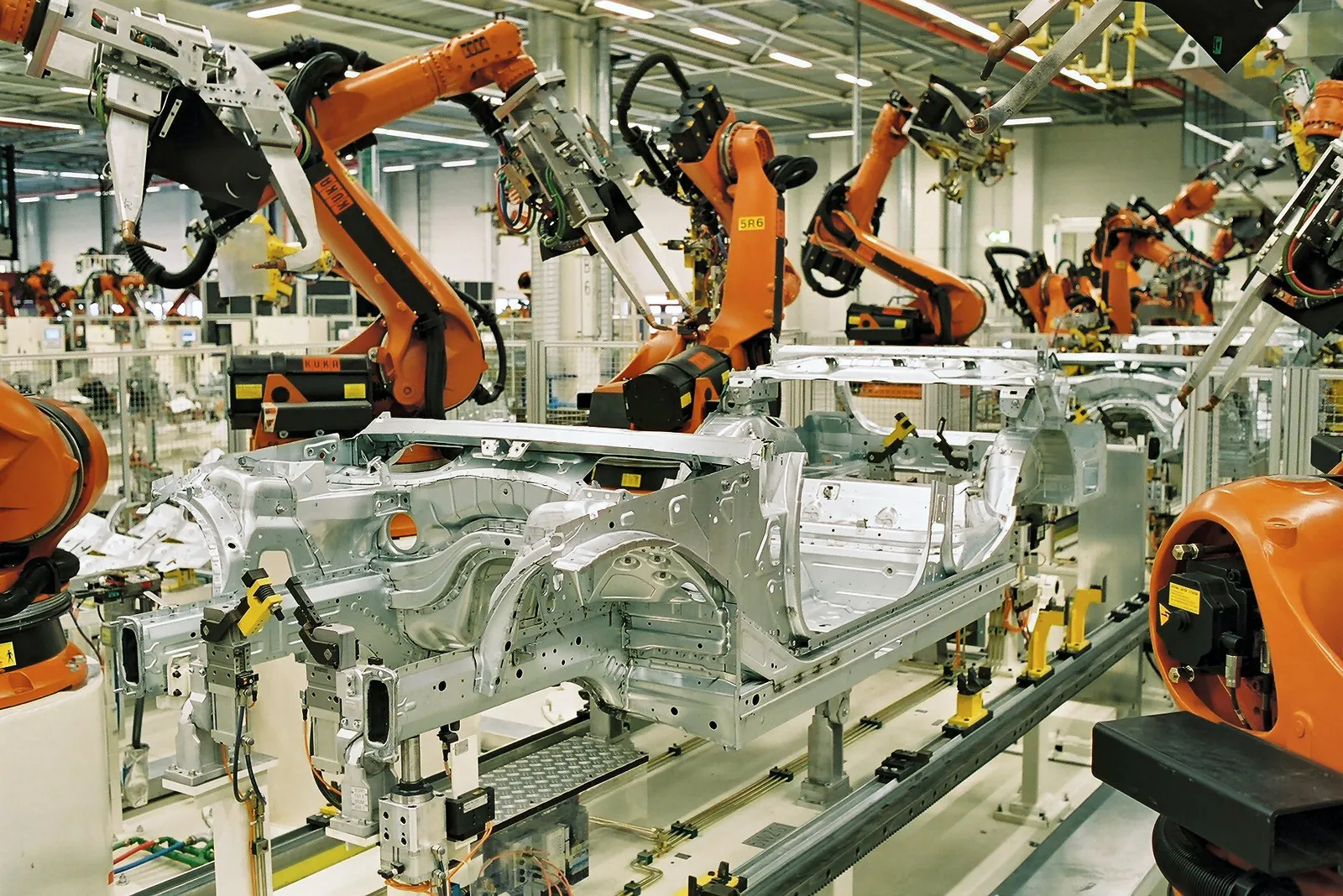 Rows of orange industrial robots welding car bodies on an assembly line