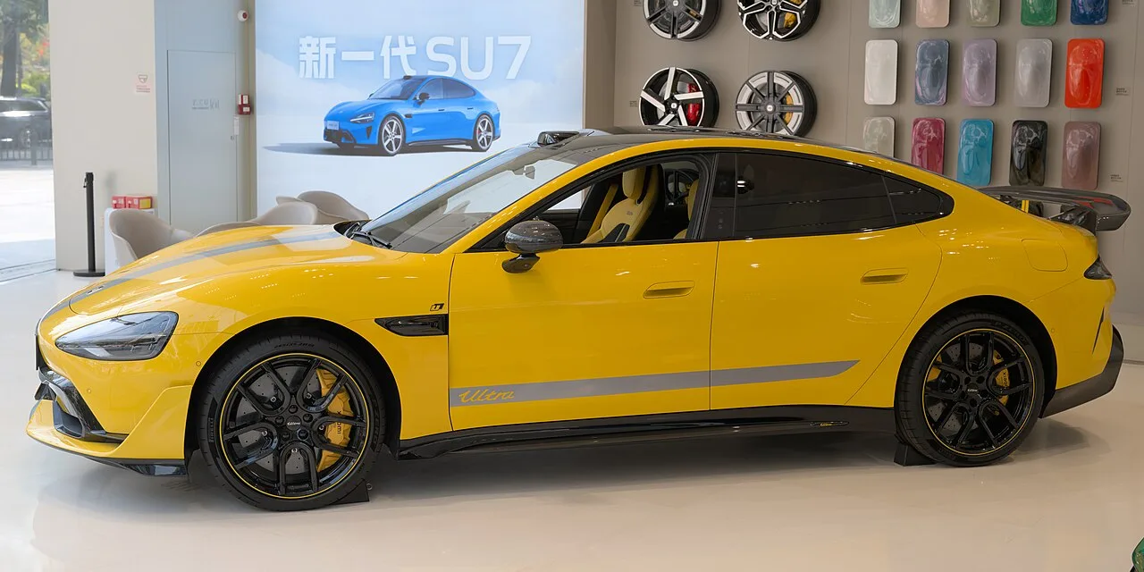 Yellow Xiaomi SU7 Ultra with a rear wing in a showroom, side view